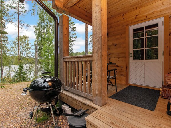 A wooden deck with a barbecue grill, a door, and a view of trees and a body of water.