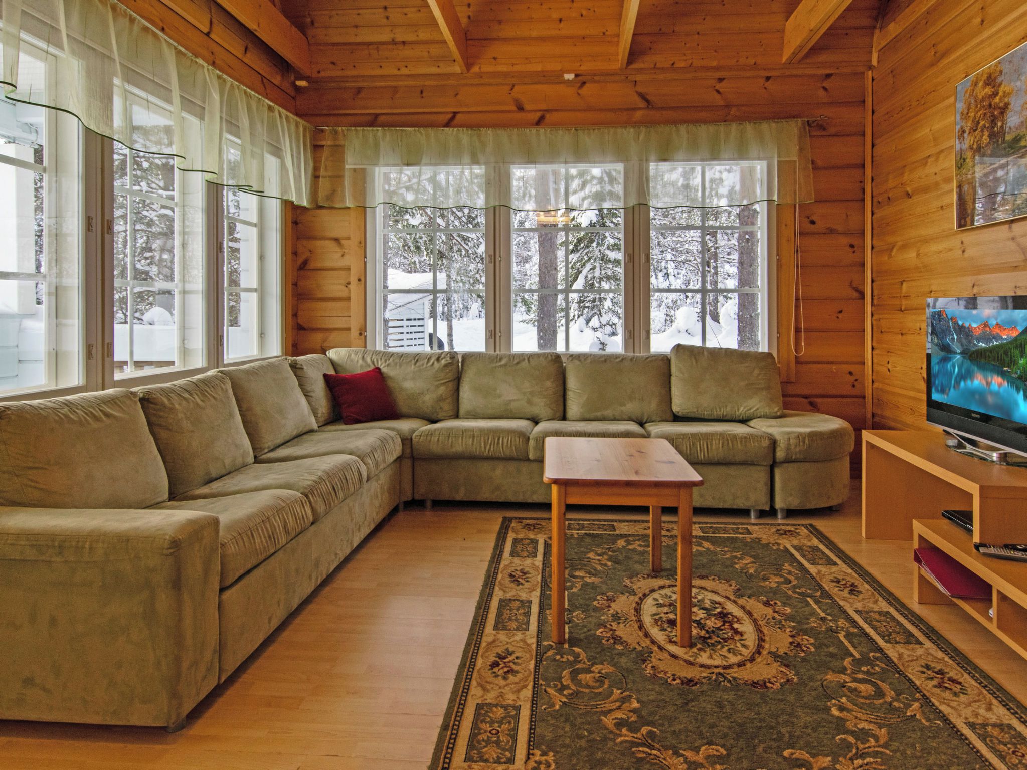 Una sala de estar acogedora con un sofá modular, una pequeña mesa de centro de madera y un televisor sobre un mueble de madera.