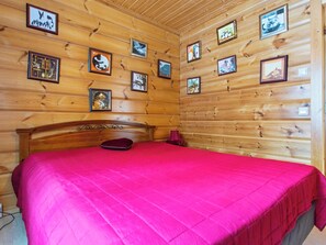 Une pièce aux murs lambrissés, avec un lit, une tête de lit en bois et plusieurs tableaux encadrés.