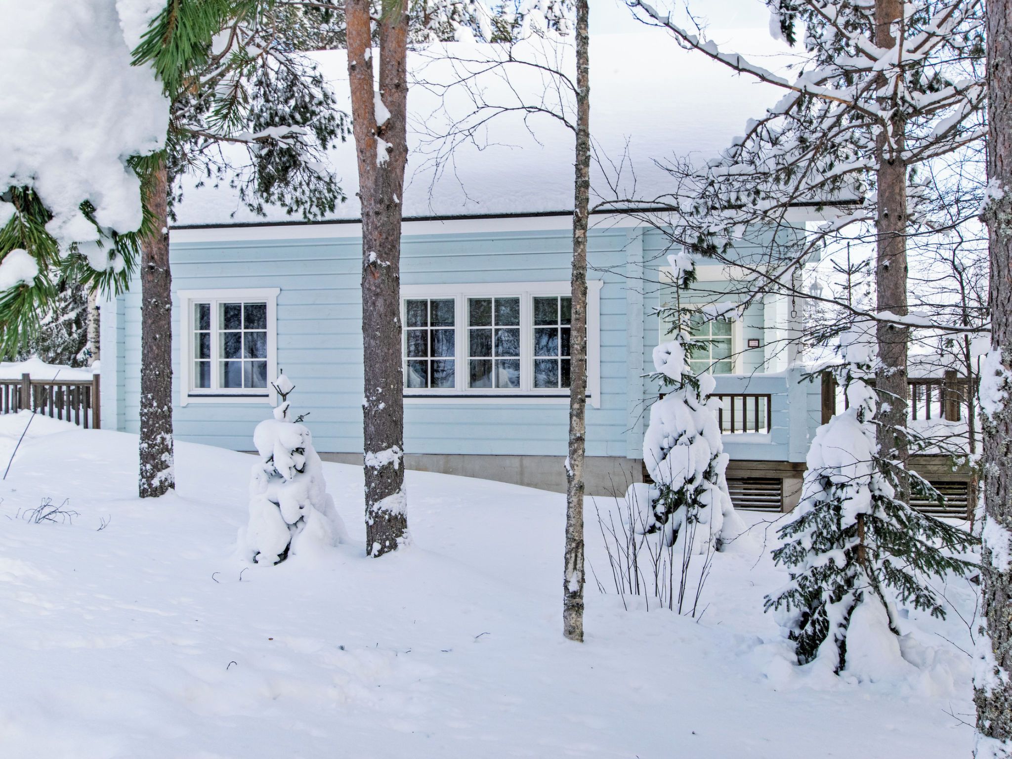 Un bâtiment bleu clair, entouré d’arbres couverts de neige et d’une clôture en bois.