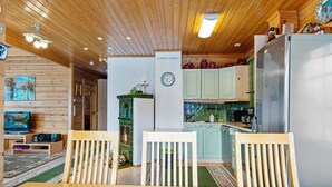A cozy cabin interior with a wooden dining table, two chairs, a kitchen with light green cabinets, and a large window. - Lomataivas mökki by Interhome (Hyrynsalmi)