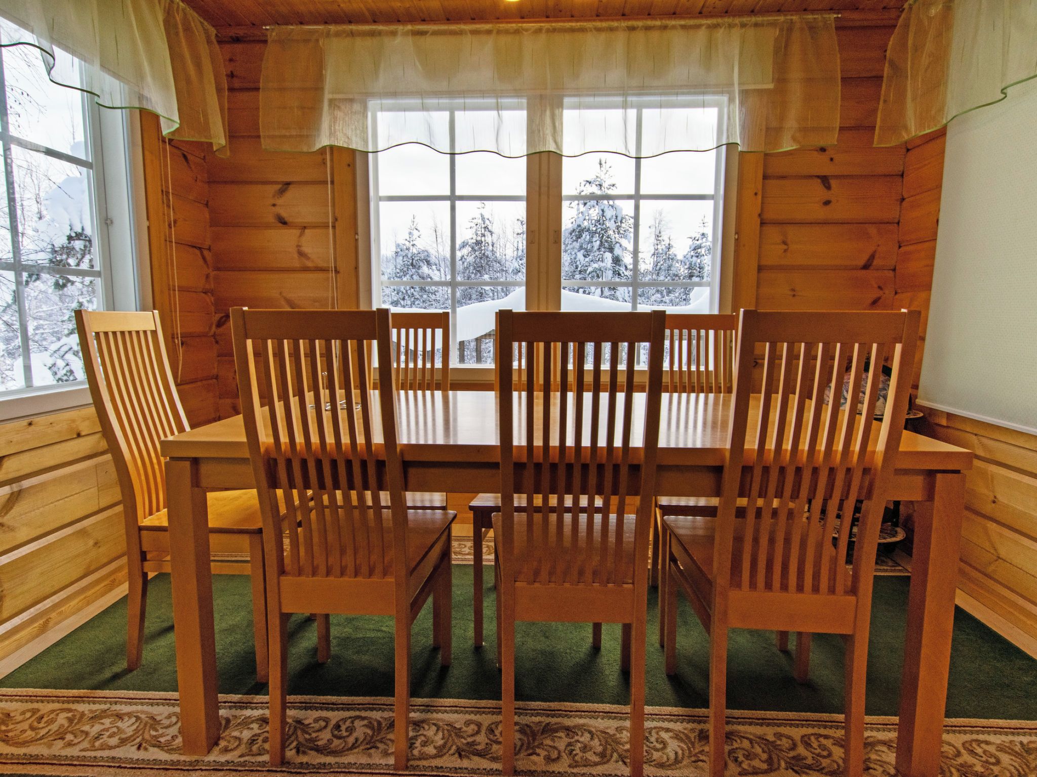 A wooden dining table with four chairs, set on a green carpet with a patterned border.