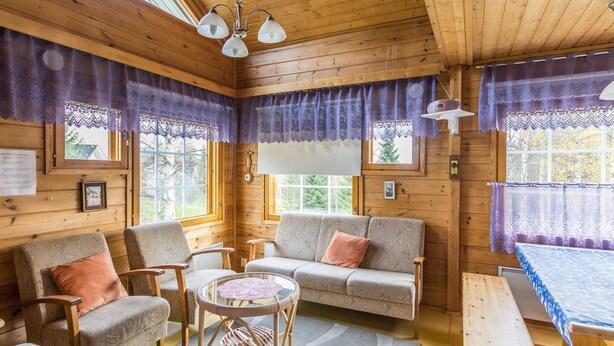 A cozy cabin interior with wooden walls, a sofa, chairs, a small table, and a bench. - Lomaluola 5a paritalo by Interhome (Hyrynsalmi)