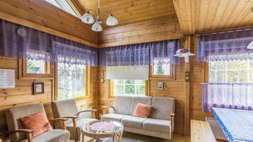 Interior acolhedor de uma cabana com paredes de madeira, um sofá, cadeiras, uma mesa e uma cama.