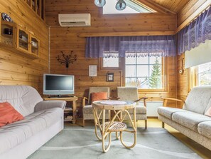 Een gezellig interieur van een chalet met een televisie, twee banken, een rieten tafeltje en een raam met uitzicht op bomen.