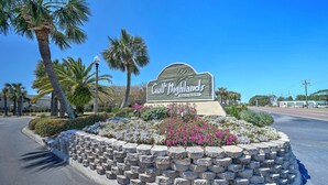 Schild für das Gulf Highlands Beach Resort, umgeben von einer angelegten Grünfläche mit Palmen und blühenden Pflanzen.
