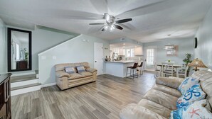 Ein geräumiges Wohnzimmer mit einem beigefarbenen Ledersofa, Deckenventilator und Holzdielen.