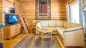 A cozy cabin interior with a wooden interior, a sofa, a television, and a ladder.