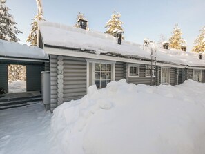 A log cabin with a snow-covered roof and a large pile of snow in front.