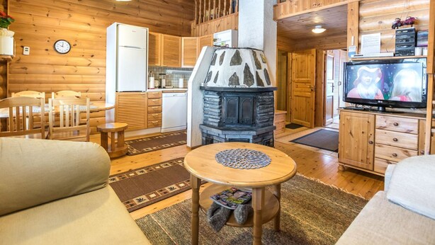 A cozy cabin interior with a stone fireplace, wooden furniture, and a television.