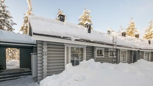 A log cabin with a snow-covered roof and windows, surrounded by snow.