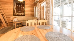 A cozy log cabin interior with a wooden dining table, two chairs, a sofa, and a large window with curtains.