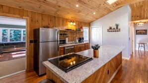 Una cocina moderna con paneles de madera, un refrigerador de acero inoxidable, una encimera de granito y una estufa empotrada.