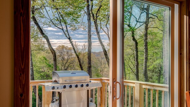 Terraza de madera con una parrilla de barbacoa y tanques de propano, con vista a un área boscosa.