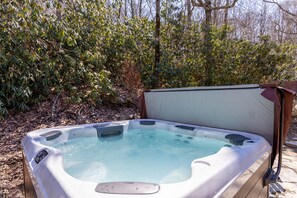 Ein Whirlpool in einer Außenanlage mit einer Holzterrasse und dichter Vegetation im Hintergrund.