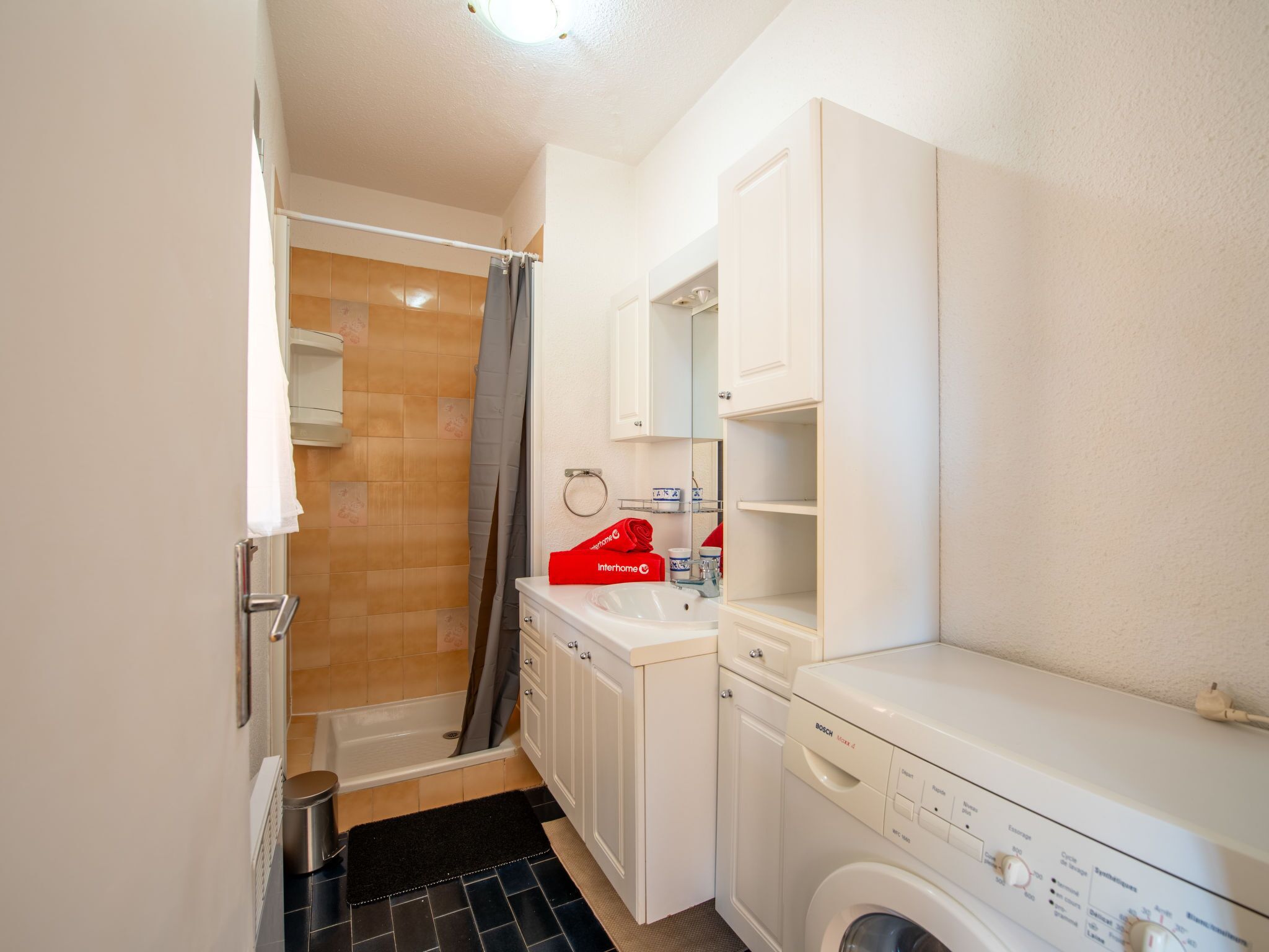 A compact bathroom with a shower, sink, and washing machine.