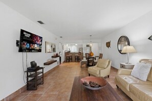 A living room with a TV, sofa, coffee table, and a dining area in the background. - Saddlebrook Resort Condo | Golf Views | King Suite | Optional Resort Amenities (Wesley Chapel)