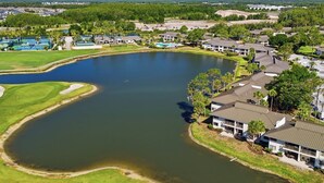 A golf course with a pond, surrounded by residential buildings and a tennis court.