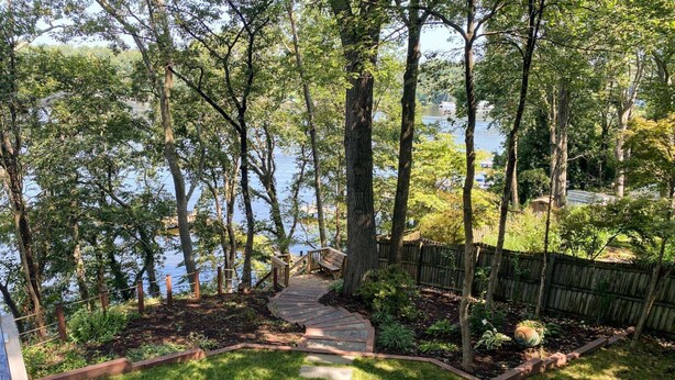 A wooden deck leading to a lake, surrounded by trees and a wooden fence.