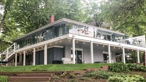 A modern two-story house with a glass balcony, a covered patio, and a well-maintained garden.