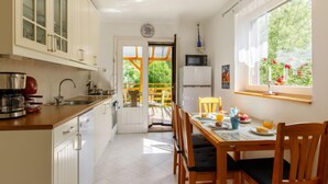 Une cuisine avec des meubles blancs, une table à manger avec des chaises, une fenêtre donnant sur un espace verdoyant et un four à micro-ondes.