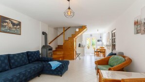 Un salon comprenant un canapé, un fauteuil en osier, une table, un escalier et un coin cuisine.