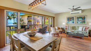 A spacious living area with a wooden dining table, a sofa set, and a balcony with a view of the ocean. - "Pacific Paradise" - Lae Nani 425 - Upgraded Second Floor 2 Bedroom | 2 Bathroom-with A/C (Kapaa)