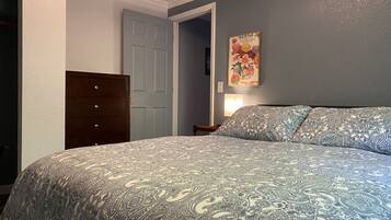 A bedroom with a bed, a dresser, a door, and a wall-mounted picture.