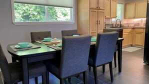 En matplats med ett bord för fyra personer, omgiven av stolar, och ett köksområde med träskåp och en diskho.
