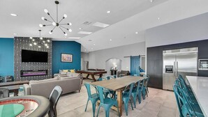 Een moderne woonkamer met een pooltafel, een open haard en een eethoek met teal stoelen.