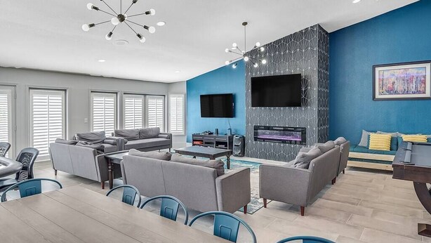 Een moderne woonkamer met een blauwe accentmuur, een flatscreen televisie aan de wand en een eethoek met een houten tafel en blauwe stoelen.