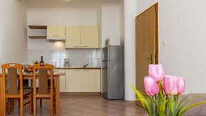 A compact kitchen with a dining area, a refrigerator, and a potted plant.