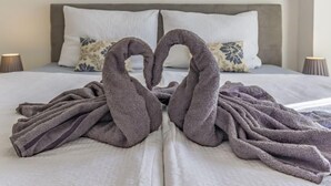 A bed with a gray blanket and two towels arranged in a heart shape.