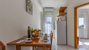 A dining area with a table set for four, a refrigerator, and a window with curtains.