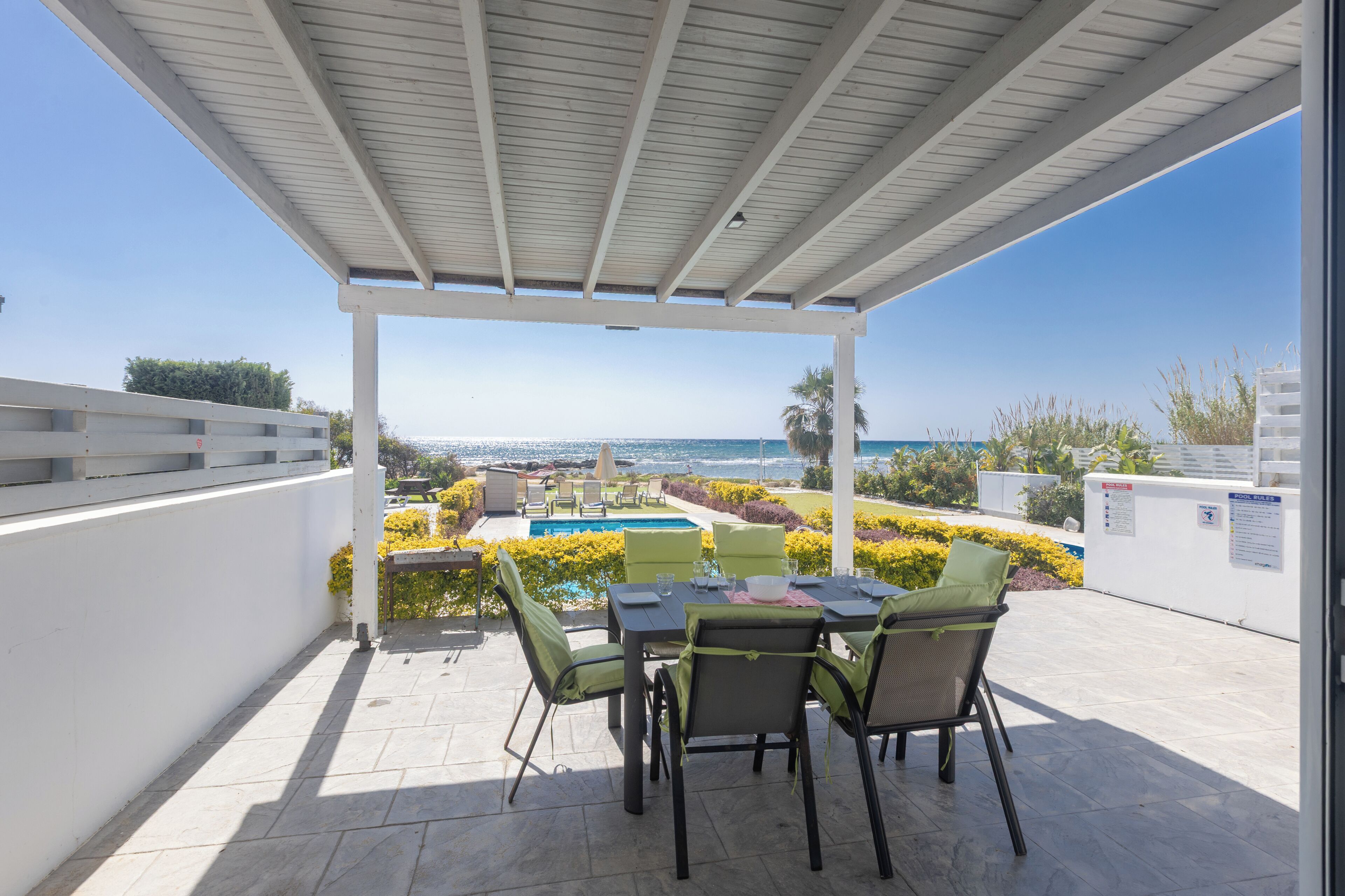 A covered outdoor patio with a pool, dining table, chairs, and a view of the sea.