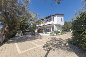 A two-story house with a balcony, surrounded by trees and a paved driveway.