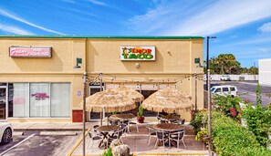 Un restaurant avec une terrasse, une enseigne indiquant « Tacos », et un salon de coiffure appelé « Frans Hair Fashion » de l’autre côté de la rue.