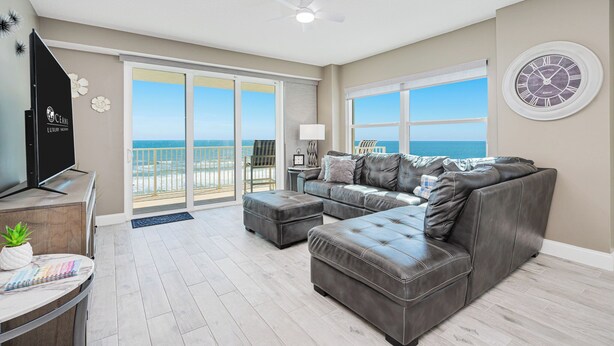 A spacious living room with a large sectional sofa, a flat-screen TV, and a balcony with a view of the ocean. - Oceanfront, Corner View - Aruba #606 (Daytona Beach Shores)