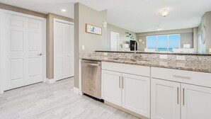 A kitchen with white cabinets, a granite countertop, and a dishwasher. - Oceanfront, Corner View - Aruba #606 (Daytona Beach Shores)