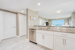 A kitchen with white cabinets, a granite countertop, and a dishwasher. - Oceanfront, Corner View - Aruba #606 (Daytona Beach Shores)