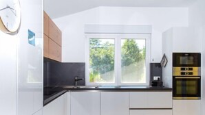 A modern kitchen with white cabinets, a black countertop, a double sink, and a built-in oven. - Francois by Interhome (Balatonbereny)