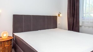 A bedroom with a bed, a nightstand, a wall-mounted lamp, and a window with curtains. - Francois by Interhome (Balatonbereny)
