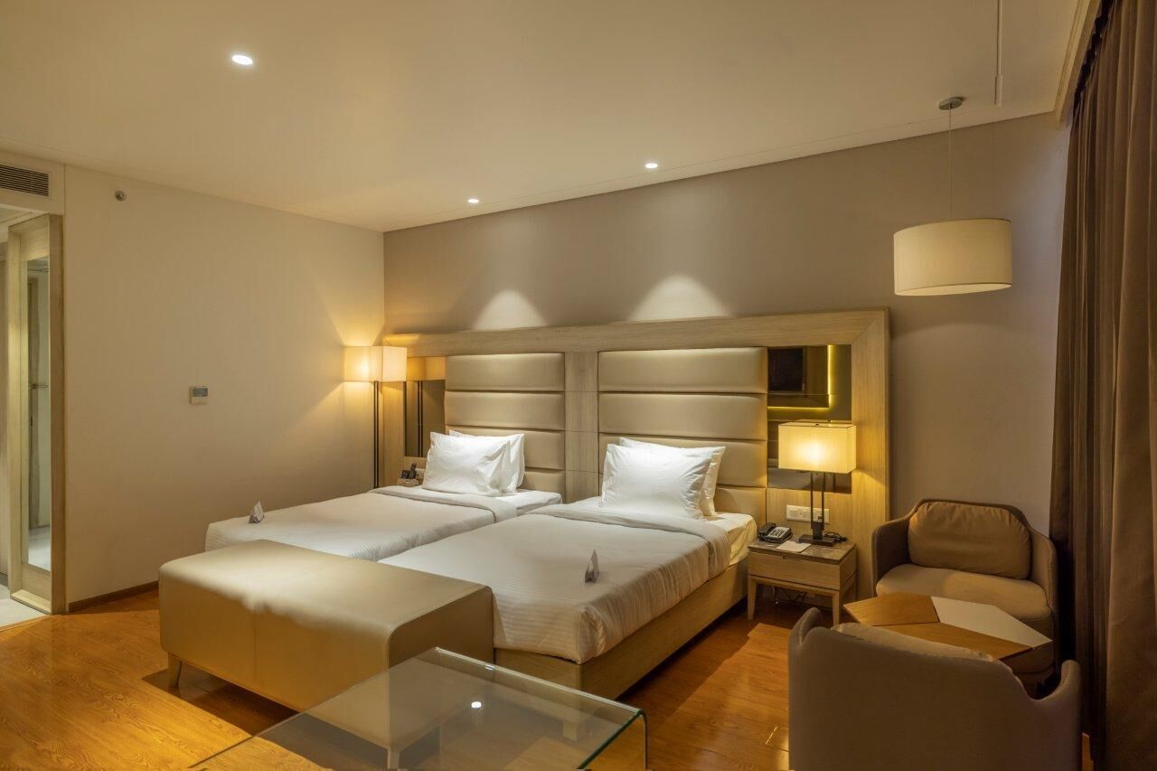 Ein Hotelzimmer mit zwei Betten, einem Schreibtisch, einem Stuhl und einem Glastisch.
