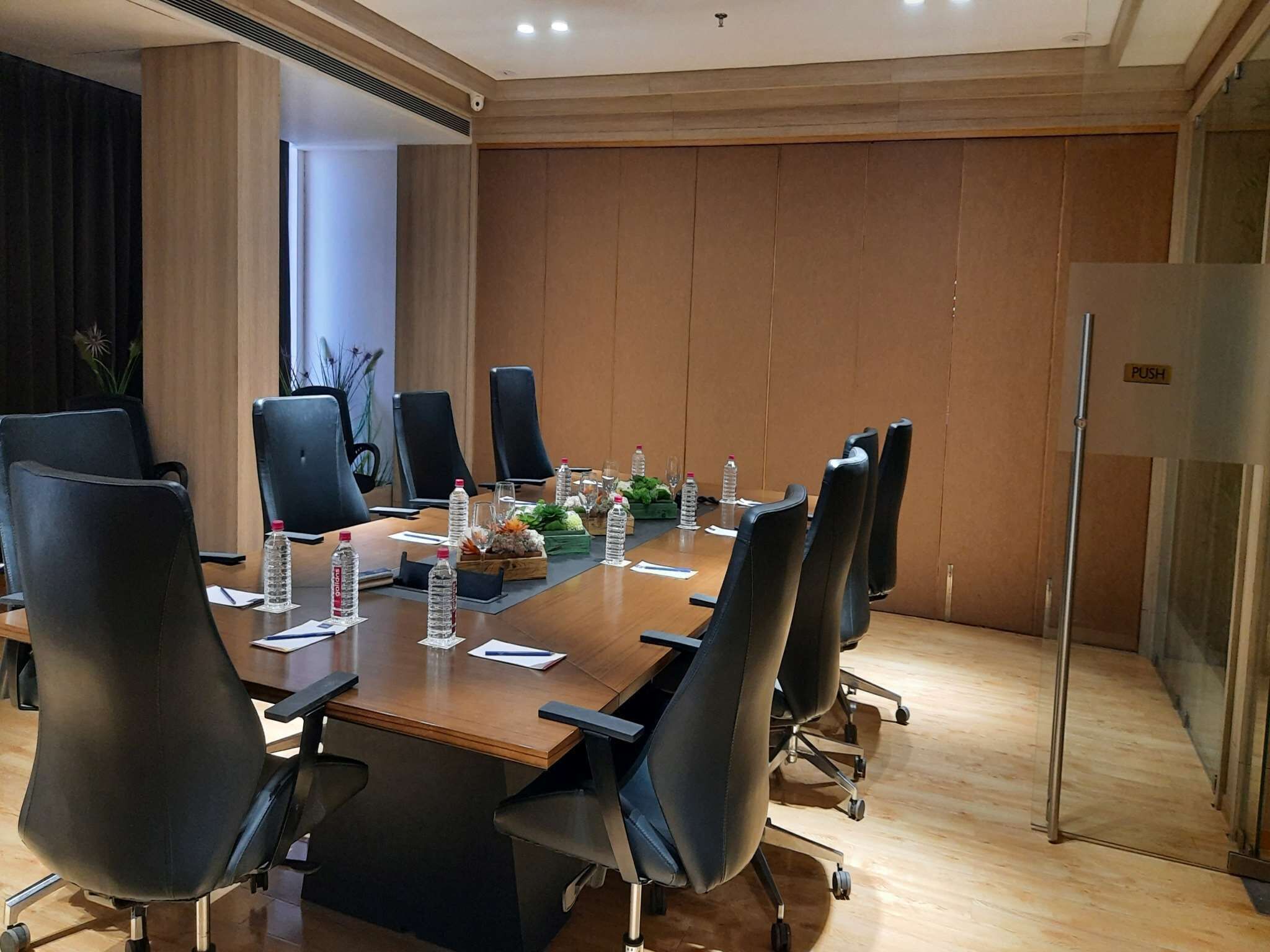 Une salle de conférence avec une longue table, des chaises noires, des bouteilles d’eau et une pancarte « POUSSER » sur la porte.