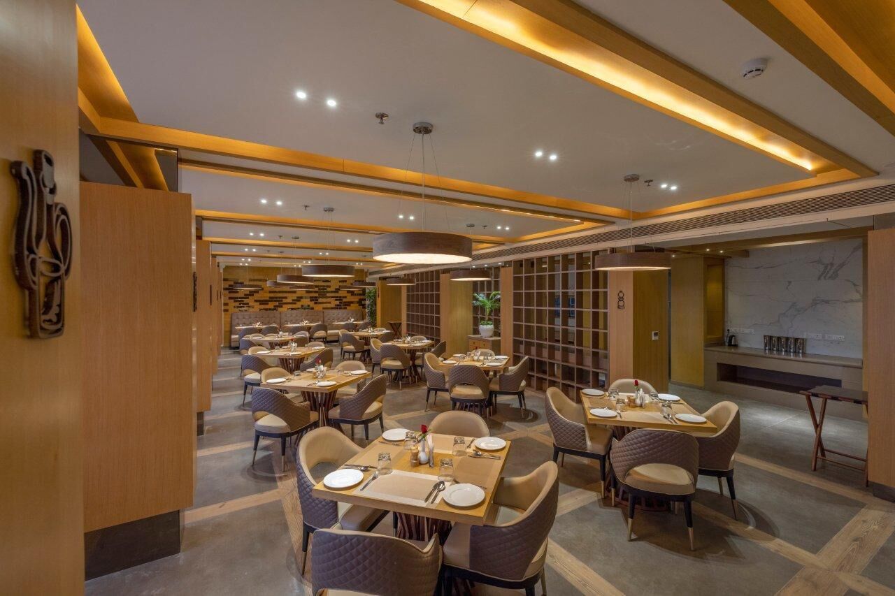 Un restaurante moderno con varias mesas y sillas, iluminación cálida y una pared de mármol.