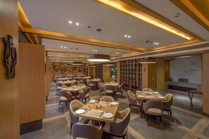 A modern restaurant with multiple dining tables and chairs, warm lighting, and a marble wall. - Sarovar Portico Morbi (Morbi)