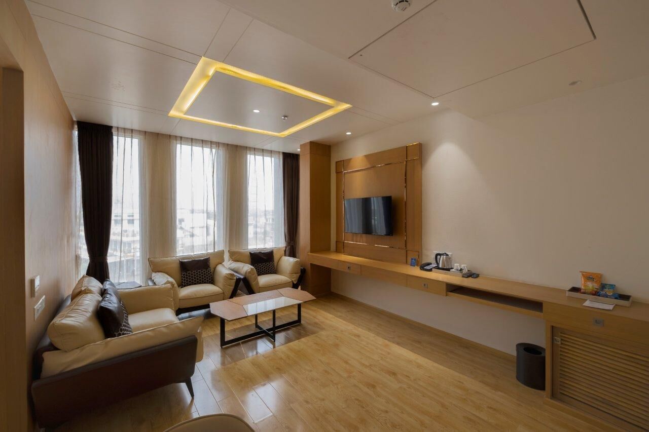 Un salon moderne comprenant un ensemble de canapés, une table basse, un téléviseur fixé sur un panneau en bois et une fenêtre avec des rideaux.
