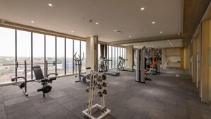 Une salle de sport spacieuse, dotée de divers équipements d’exercice, de grandes fenêtres offrant une vue sur la ville et d’un aménagement intérieur moderne.