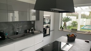 A modern kitchen with grey cabinets, a black induction cooktop, and a window with a view of a garden.
