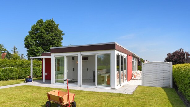 Een modern huis met een glazen deuropening, een overdekt terras en een kleine tuin.